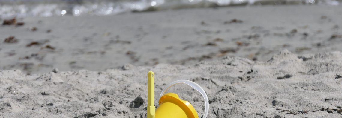 yellow plastic bucket on sand near body of water