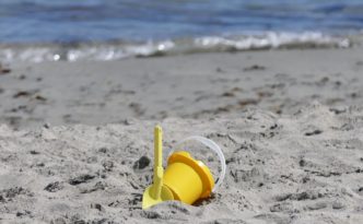 yellow plastic bucket on sand near body of water