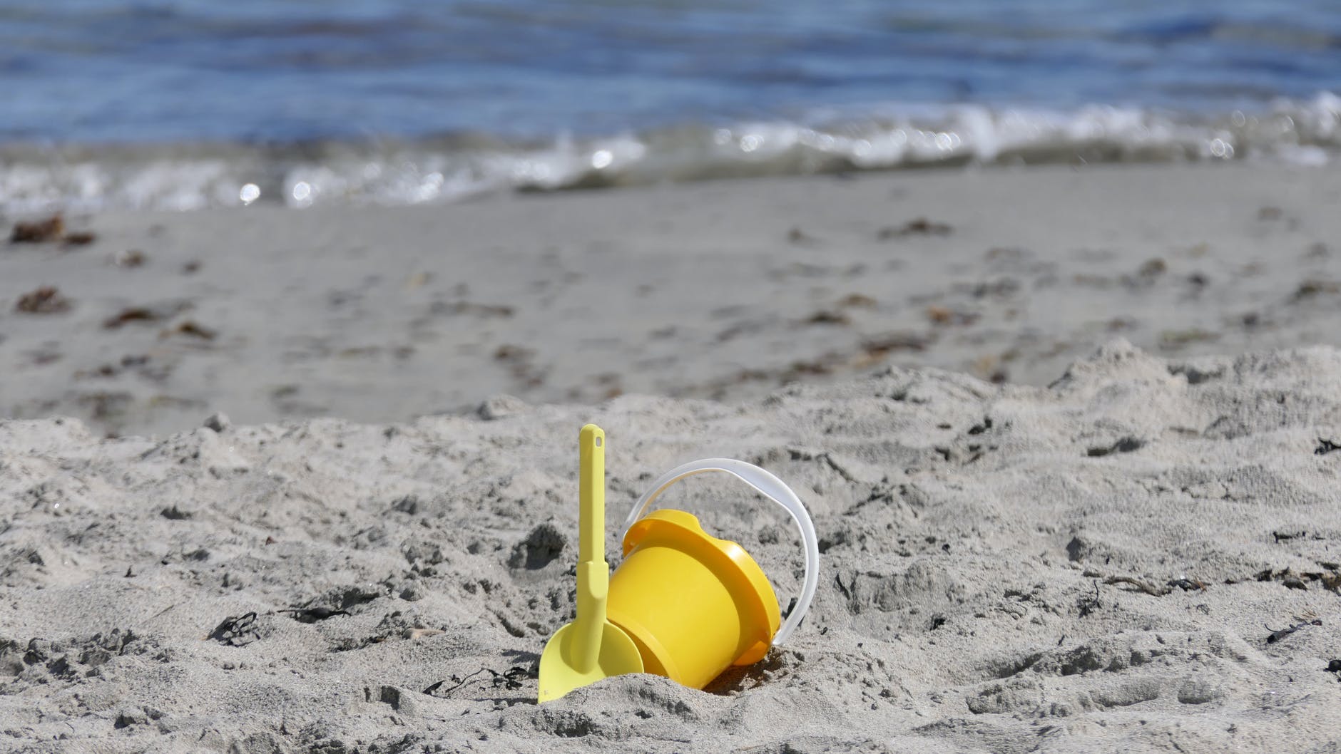 yellow plastic bucket on sand near body of water